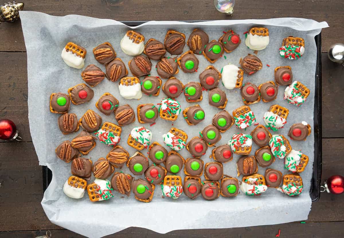 Top down shot of rolo pretzel cookies, decorated in different ways, on a parchment lined baking sheet. 