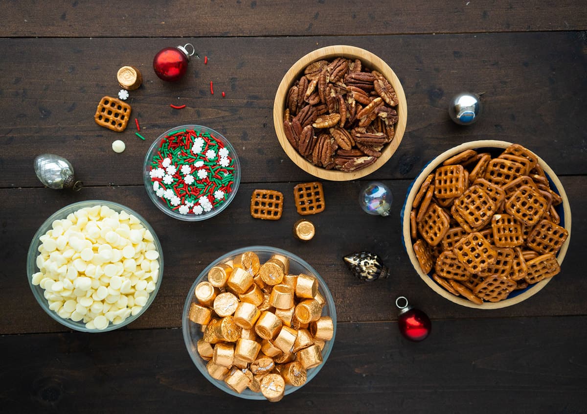 Pecans, pretzels, rolo candies, melting candy and sprinkles, all in different bowls.