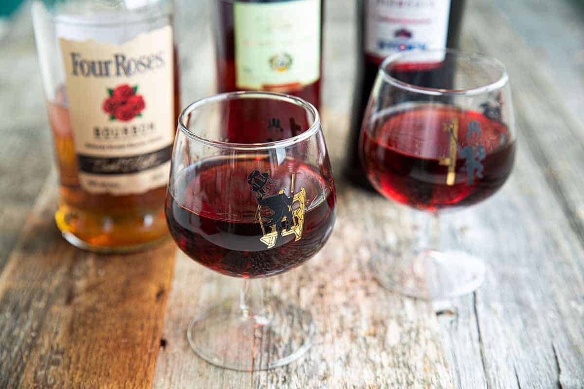 Boulevardier cocktail on a wood table with liquor bottles in the background