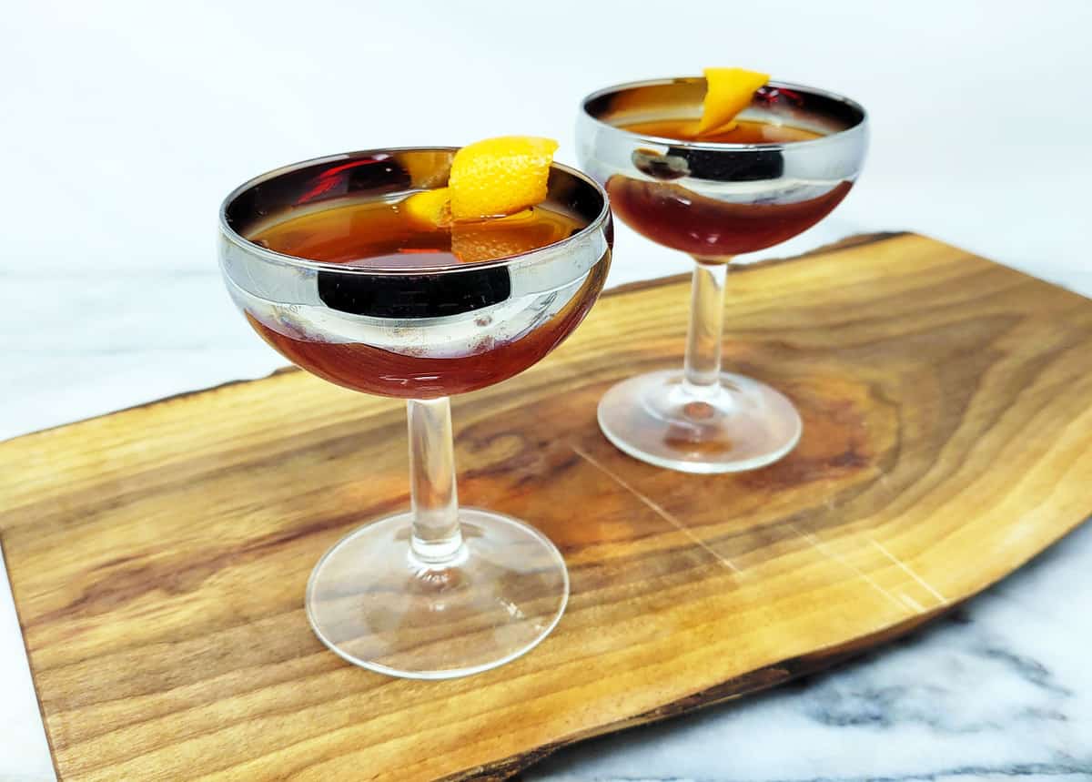 Hanky Panky cocktail in two coupe glasses in a wooden board garnished with an orange twist