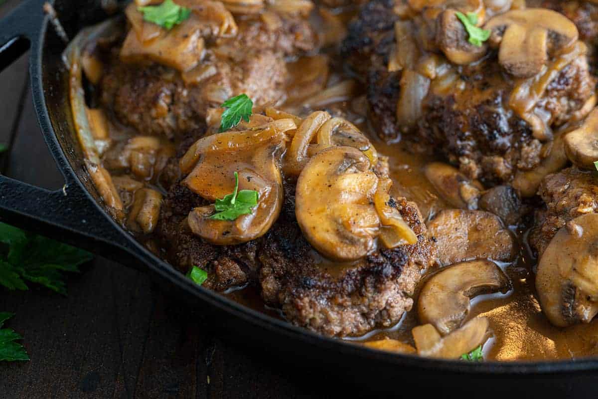 A close up of Salisbury steak, covered in mushrooms in a black pan