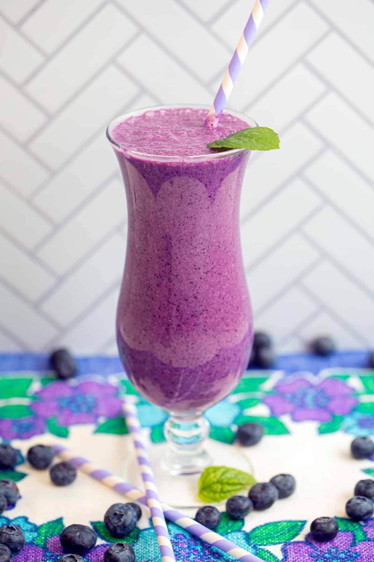 close up shot of a blueberry smoothie garnished with mine leaf on a table.
