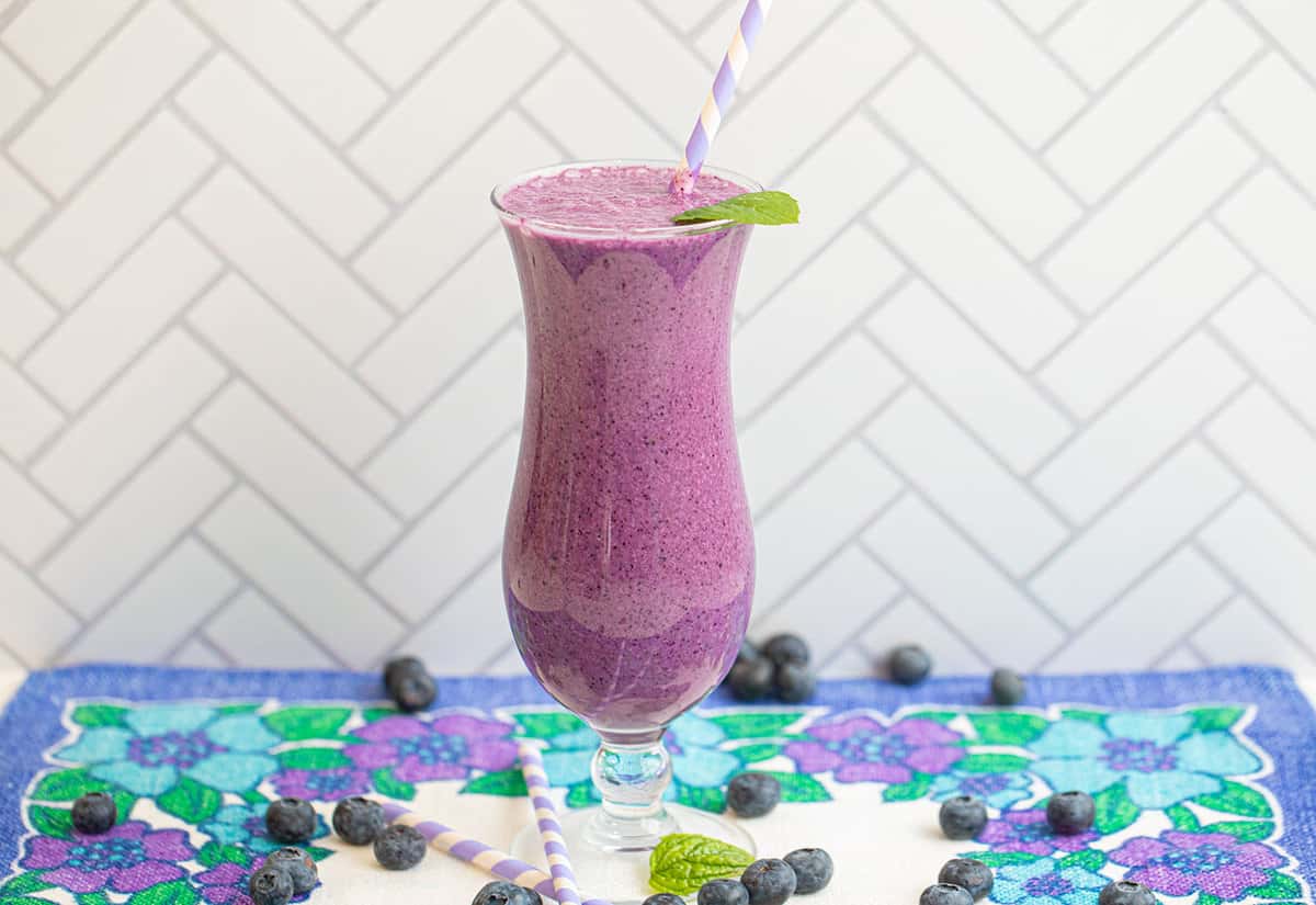 blueberry smoothie garnished with mine leaf on a table.