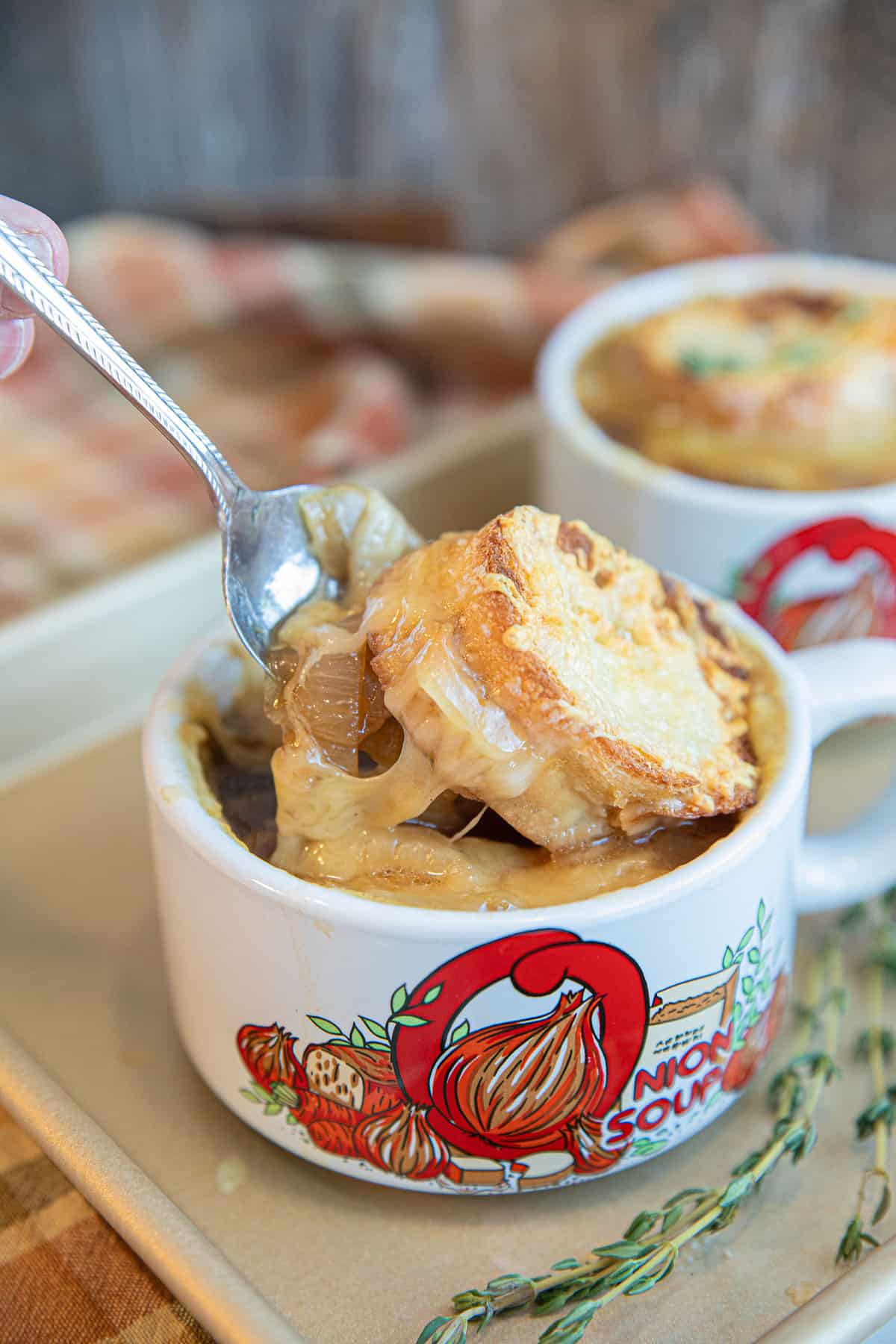 French Onion Soup in a white handled bowl with toasted cheese on top