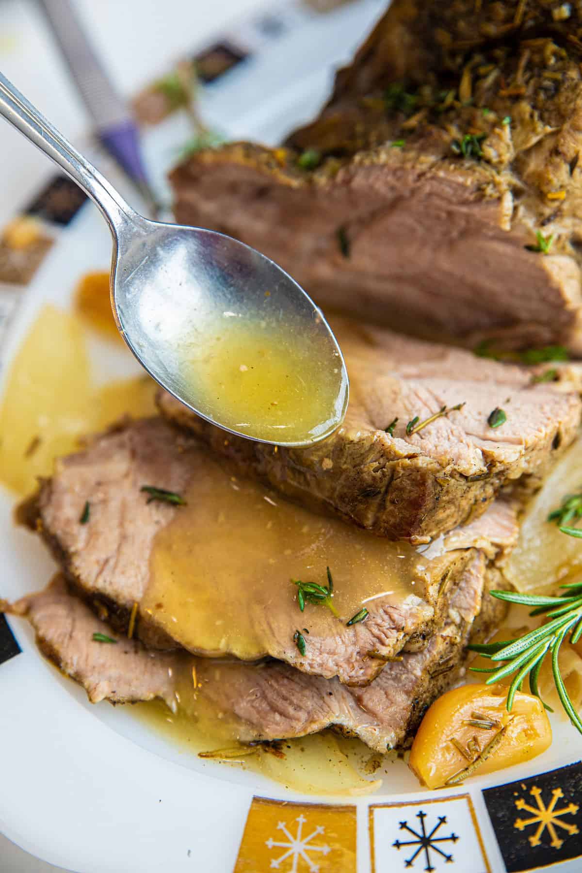 Sliced pork roast covered in juices, with a tablespoon pouring more juices over the meat.