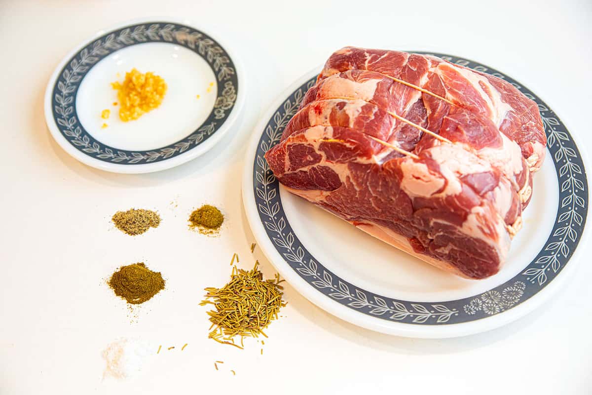 top down shot of a tied up, raw pork shoulder, with the seasoning ingredients on plates