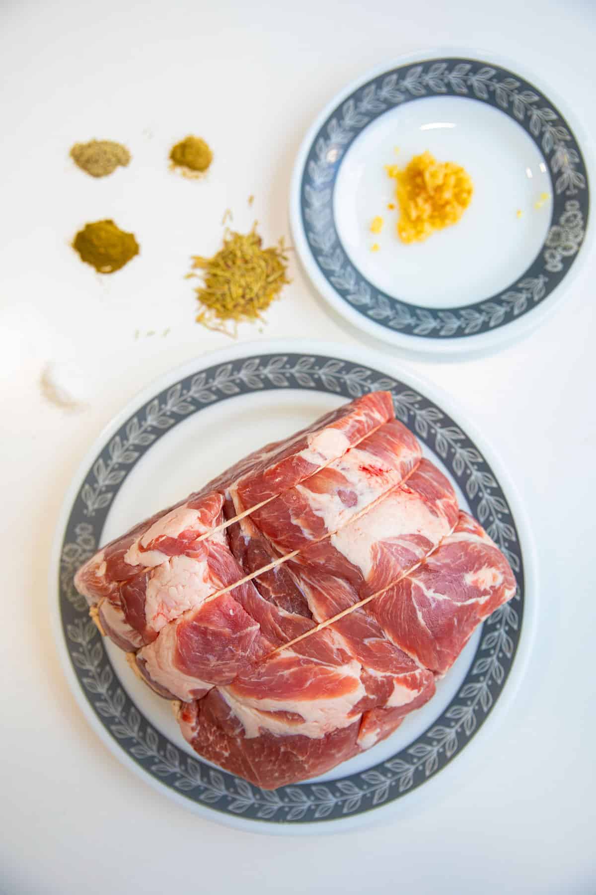 top down shot of a tied up, raw pork shoulder, with the seasoning ingredients nearby