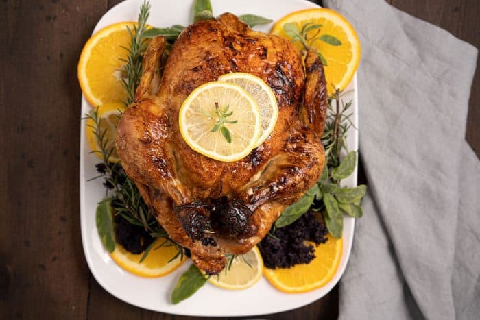 Top down shot of roast chicken on a white place topped with lemon slices and orange slices