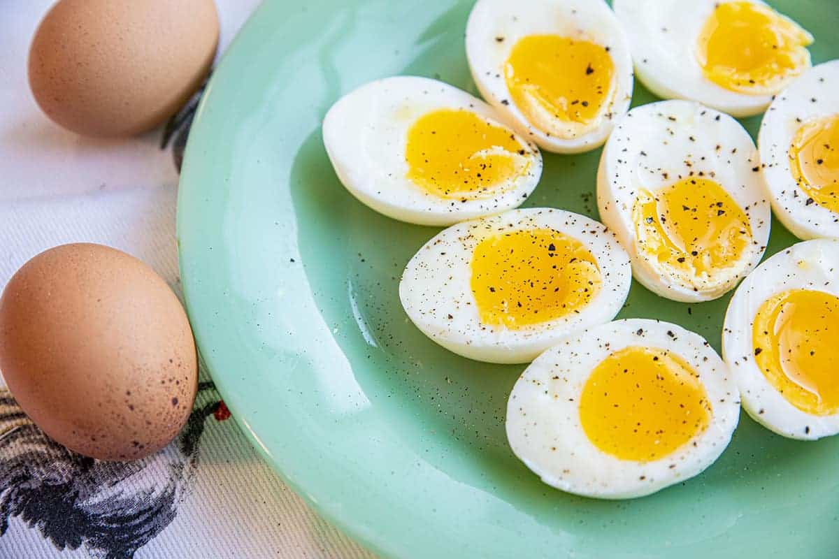 Side shot of a plate of cut in half soft boiled eggs, covered in cracked black peper 