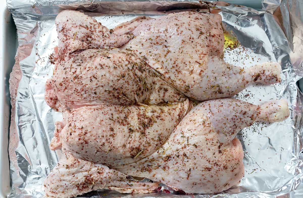 A spatchcocked chicken laying flat on a foil lined sheet pan, covered in herb butter.