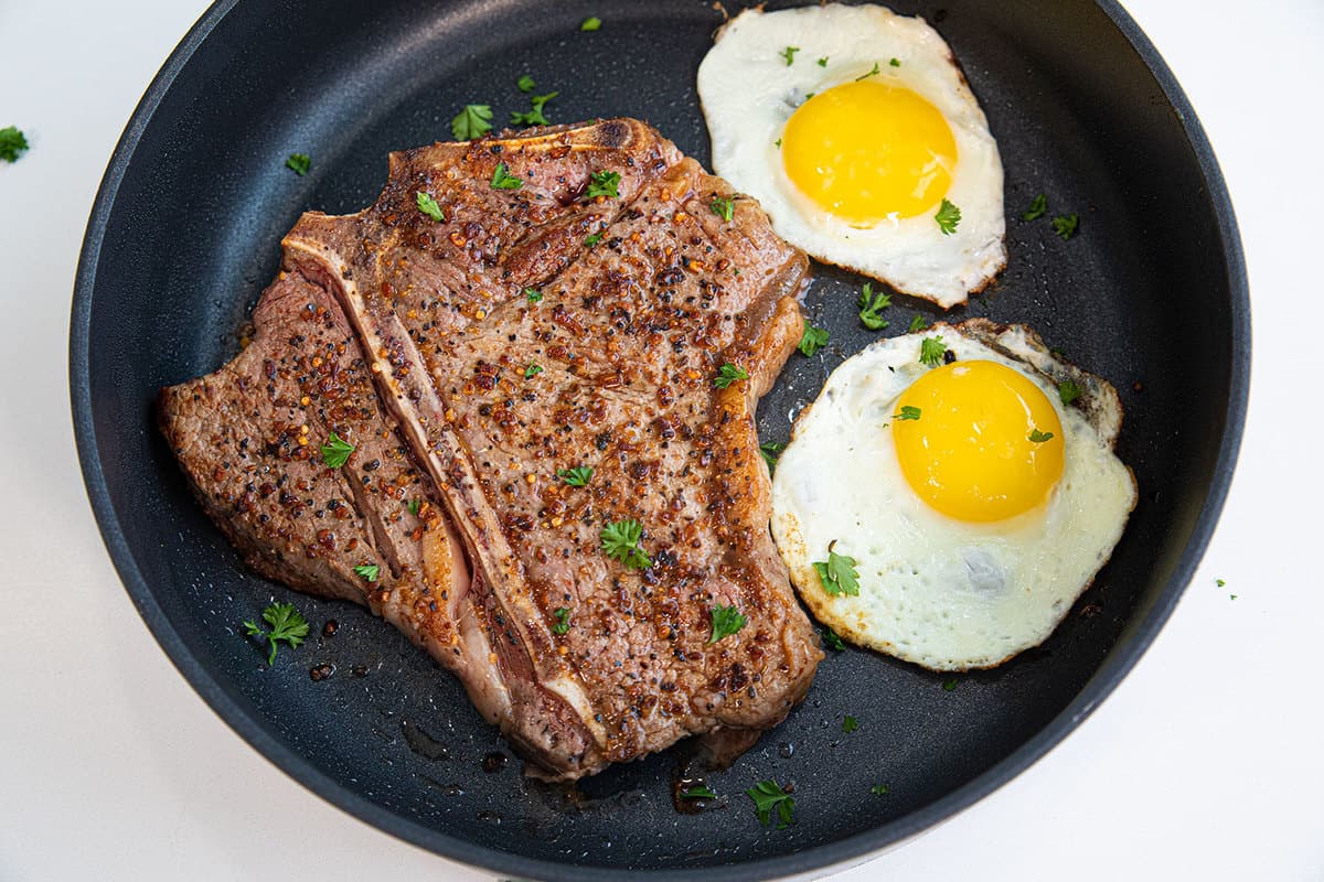 Top down shot of a t bone steak and two fried eggs on a cast iron pan