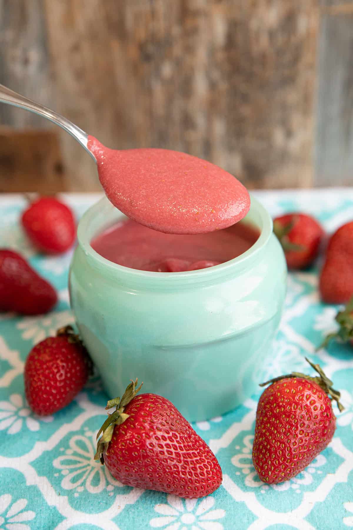 strawberry puree in a green glass jar with a spoon in it and fresh strawberries