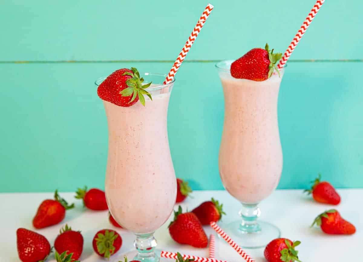 Strawberry Smoothies on a white counter, surrounded by fresh strawberries.