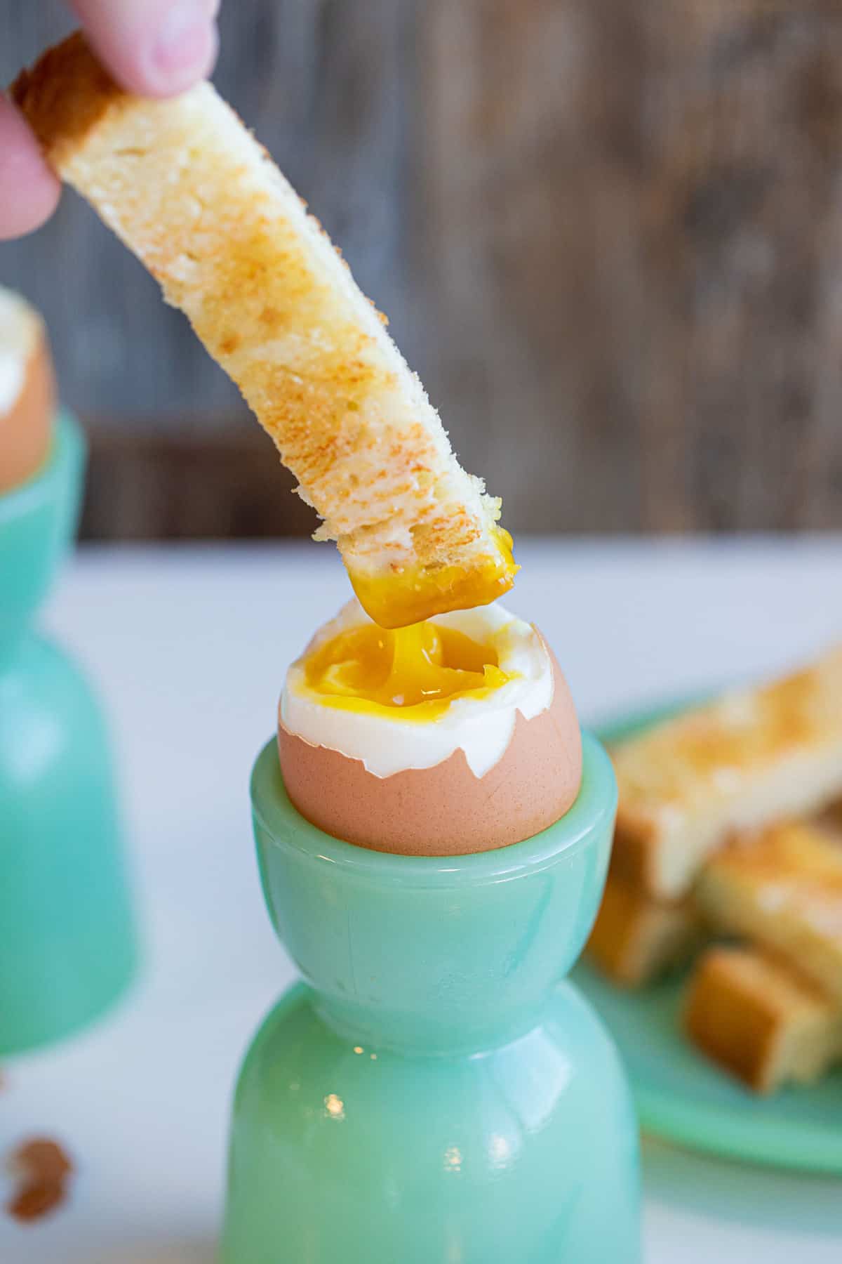 A close-up of a toast soldier being dipped into a soft boiled egg yolk