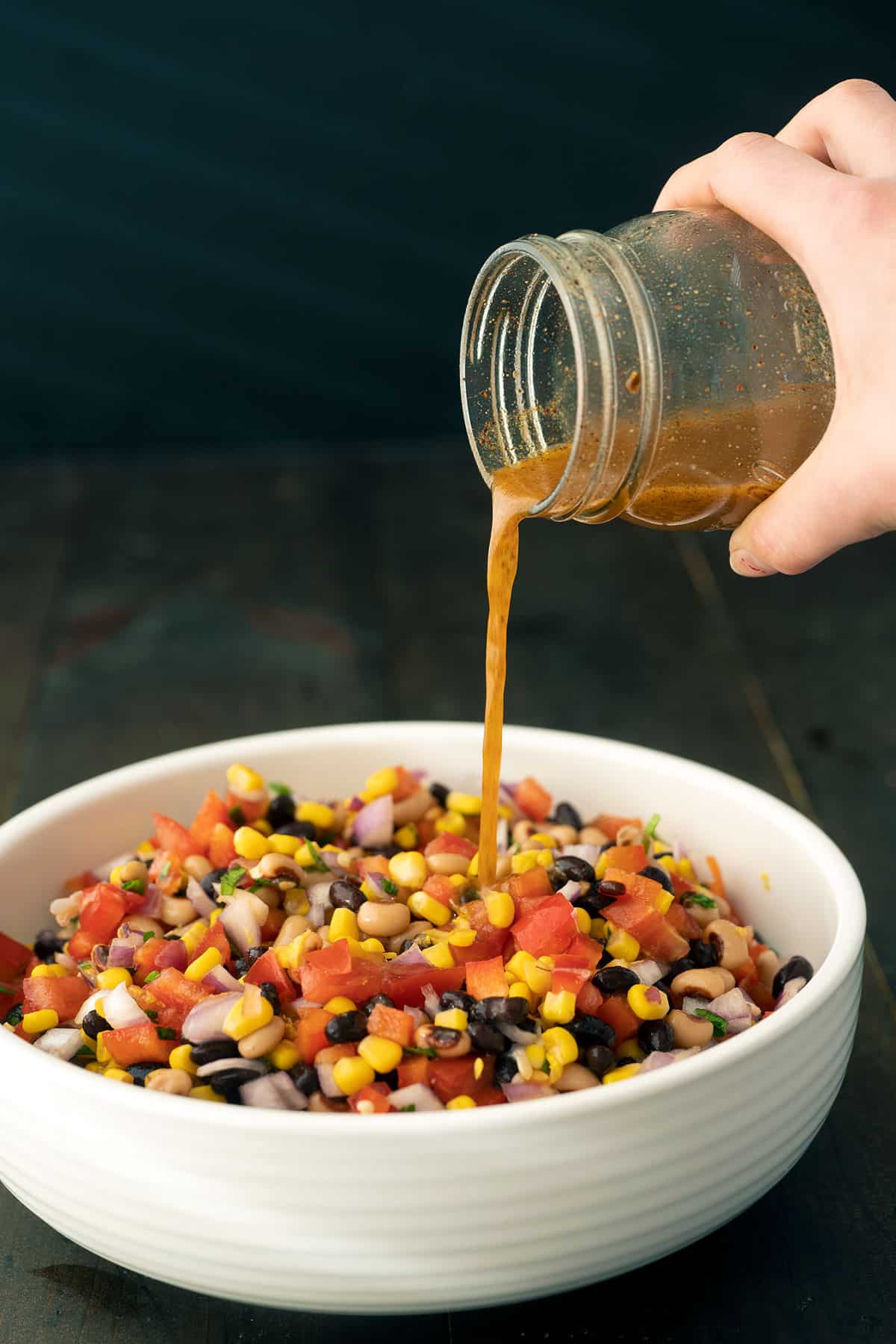 Spicy vinaigrette dressing being poured over a bowl of cowboy caviar.