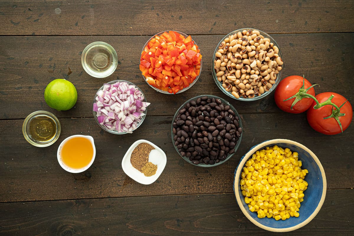 All the ingredients of cowboy caviar, seperated into glass bowls on a wooden table.