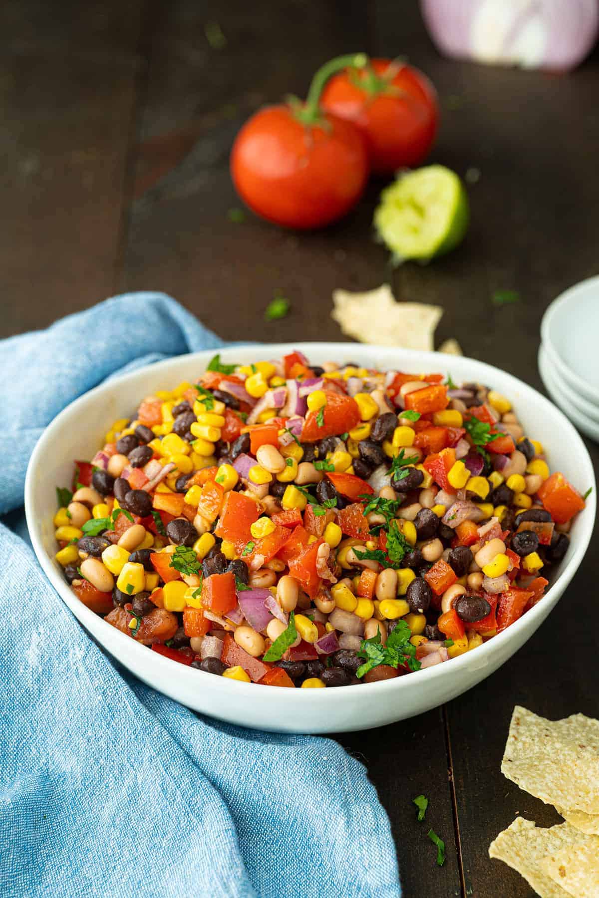 Finished bowl of cowboy caviar, topped with cilantro leaves, on a wooden table.