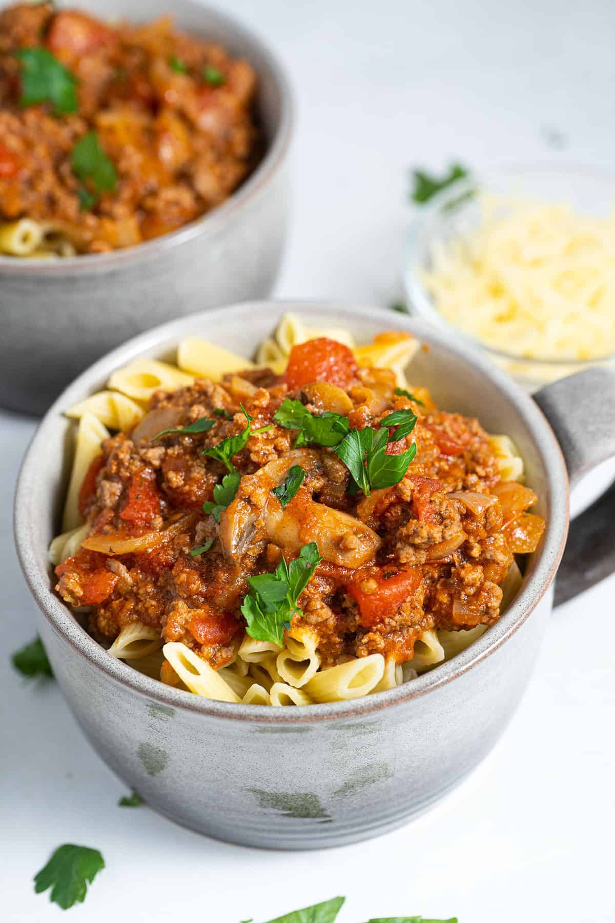 Two cupfuls of penne pasta and homemade meat sauce on a white backdrop. 