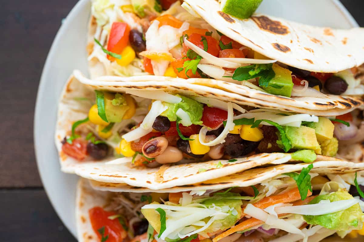 A close up of shredded chicken tacos, folded and topped with cilantro and avocado.