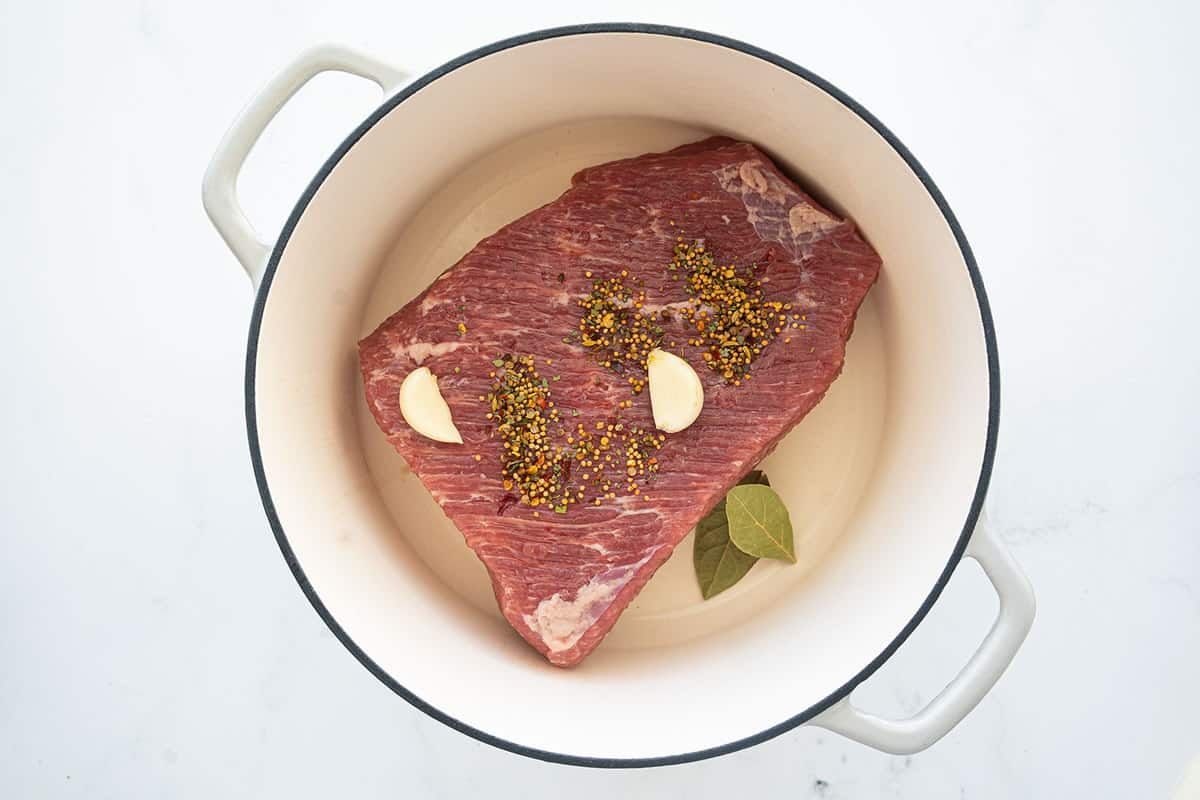 uncooked corned beef brisket and spices in a white Dutch oven