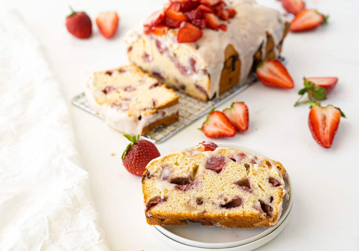 sliced strawberry bread on a plate with a loaf of strawberry bread in the background.