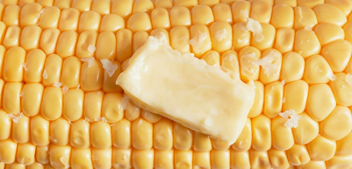 Close-up of an ear of corn with a pat of butter melting on top and sprinkled with coarse salt.