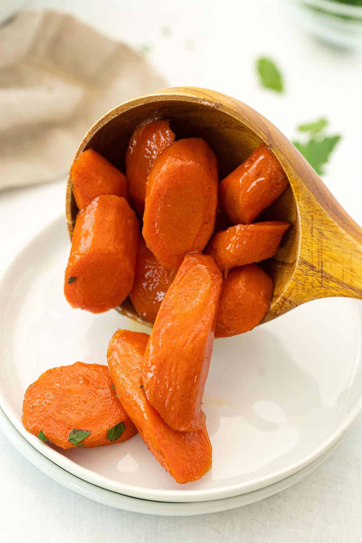 spooning candied carrots onto a white plate using a wooden spoon