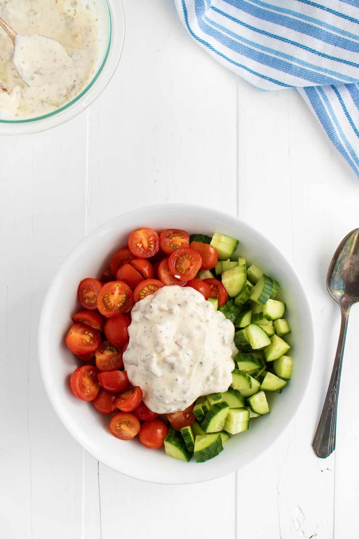 Tomatoes and cucumbers in a white bowl with Ranch dressing on top