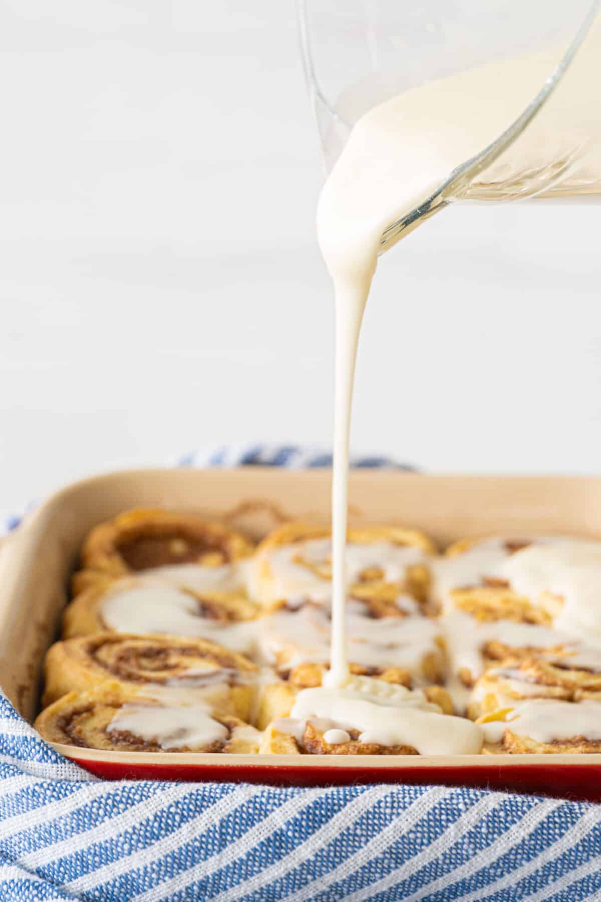 icing being poured over cinnamon rolls in a pan