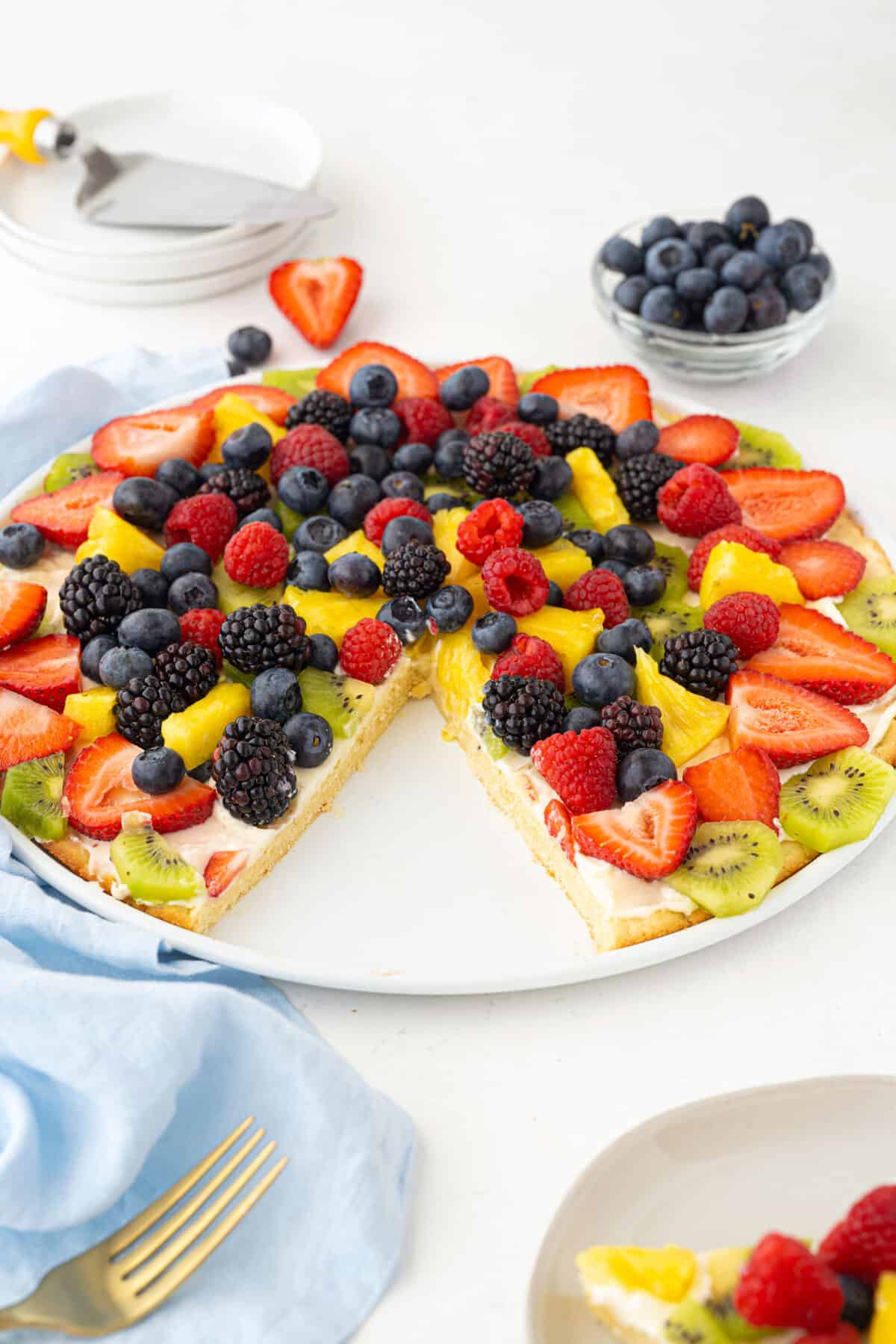 fruit pizza on a white plate with a slice taken out of it