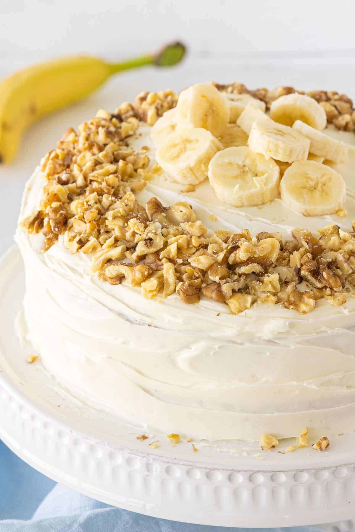 whole frosted banana cake with walnuts and fresh bananas on top
