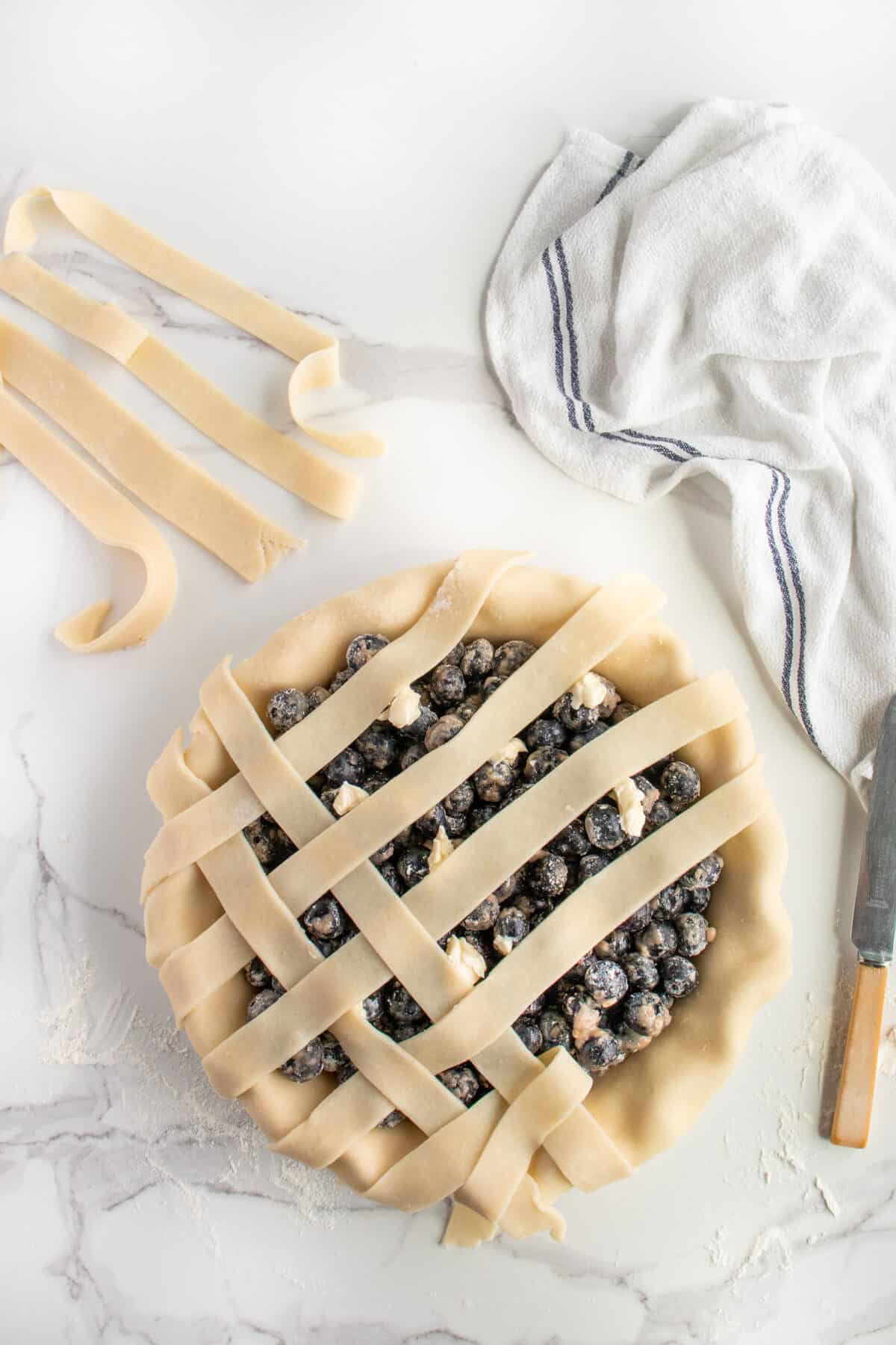 placing pie crust in a lattice pattern on top of blueberry pie