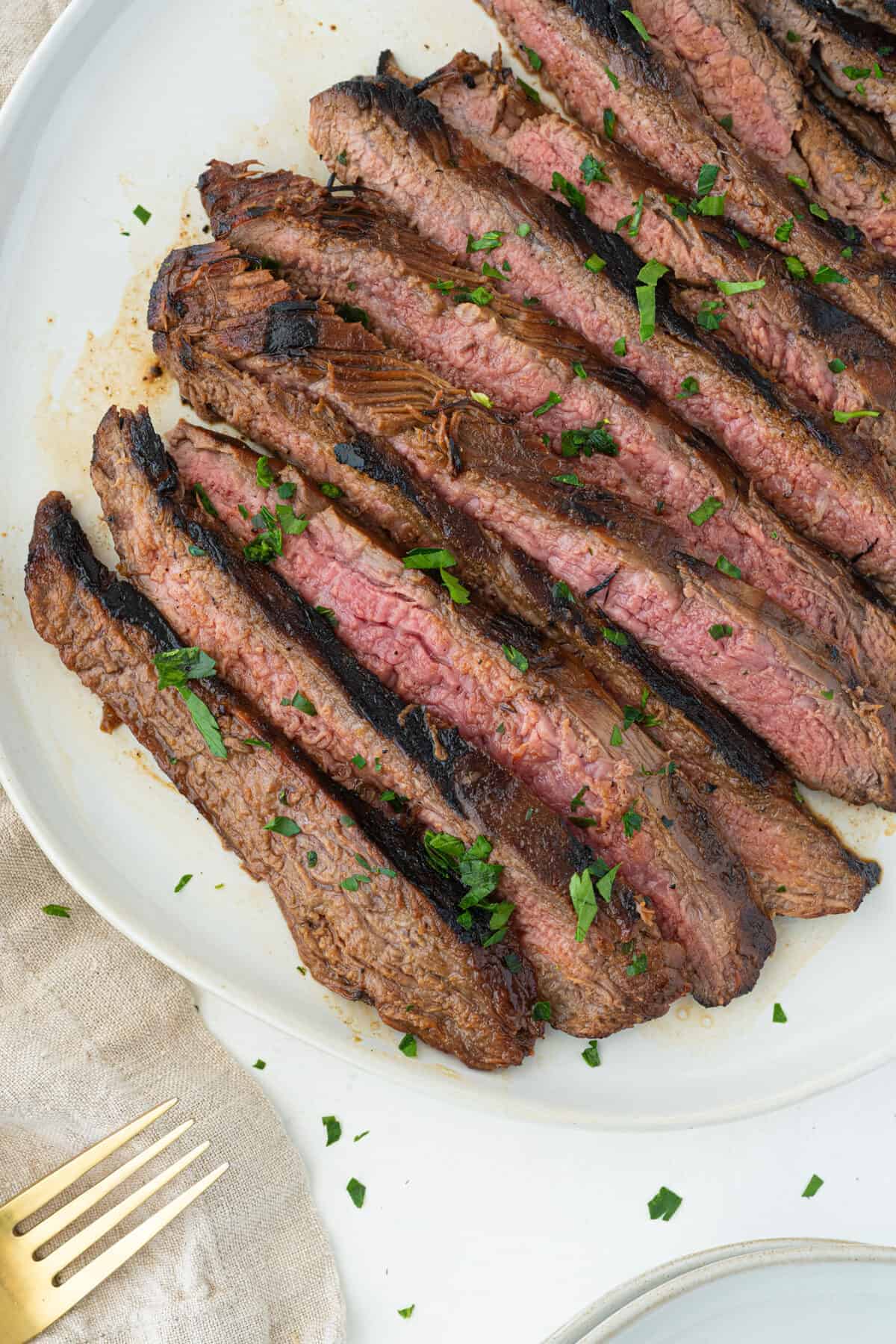 Sliced and cooked marinated flank steak on a white plate