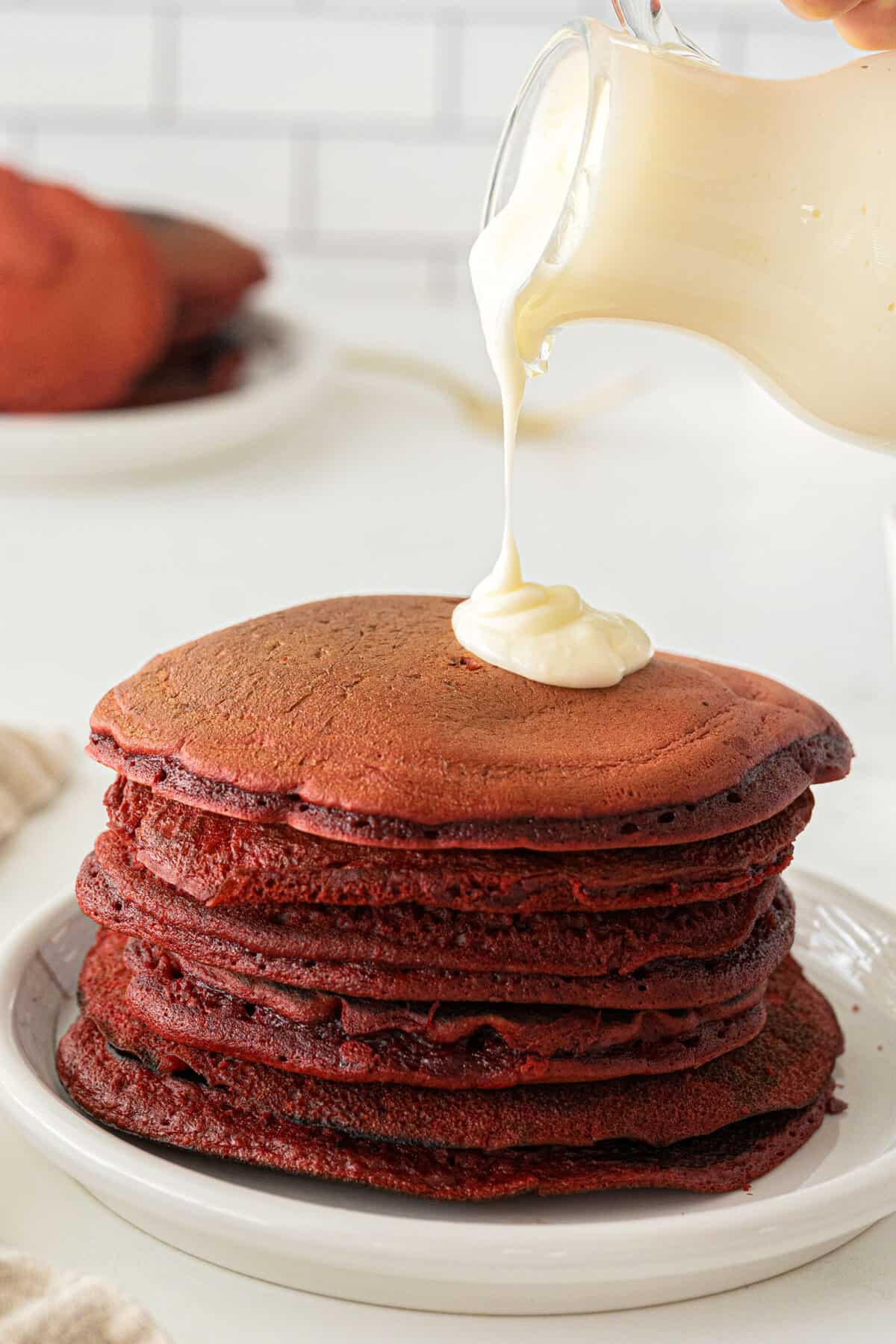 icing being poured on a stack of red velvet pancakes