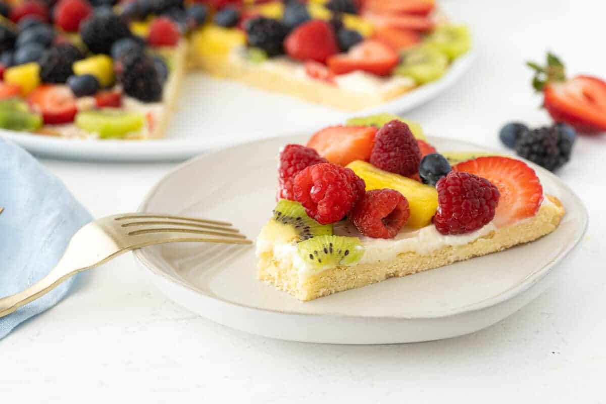 slice of fruit pizza on a white plate with a fork beside it 