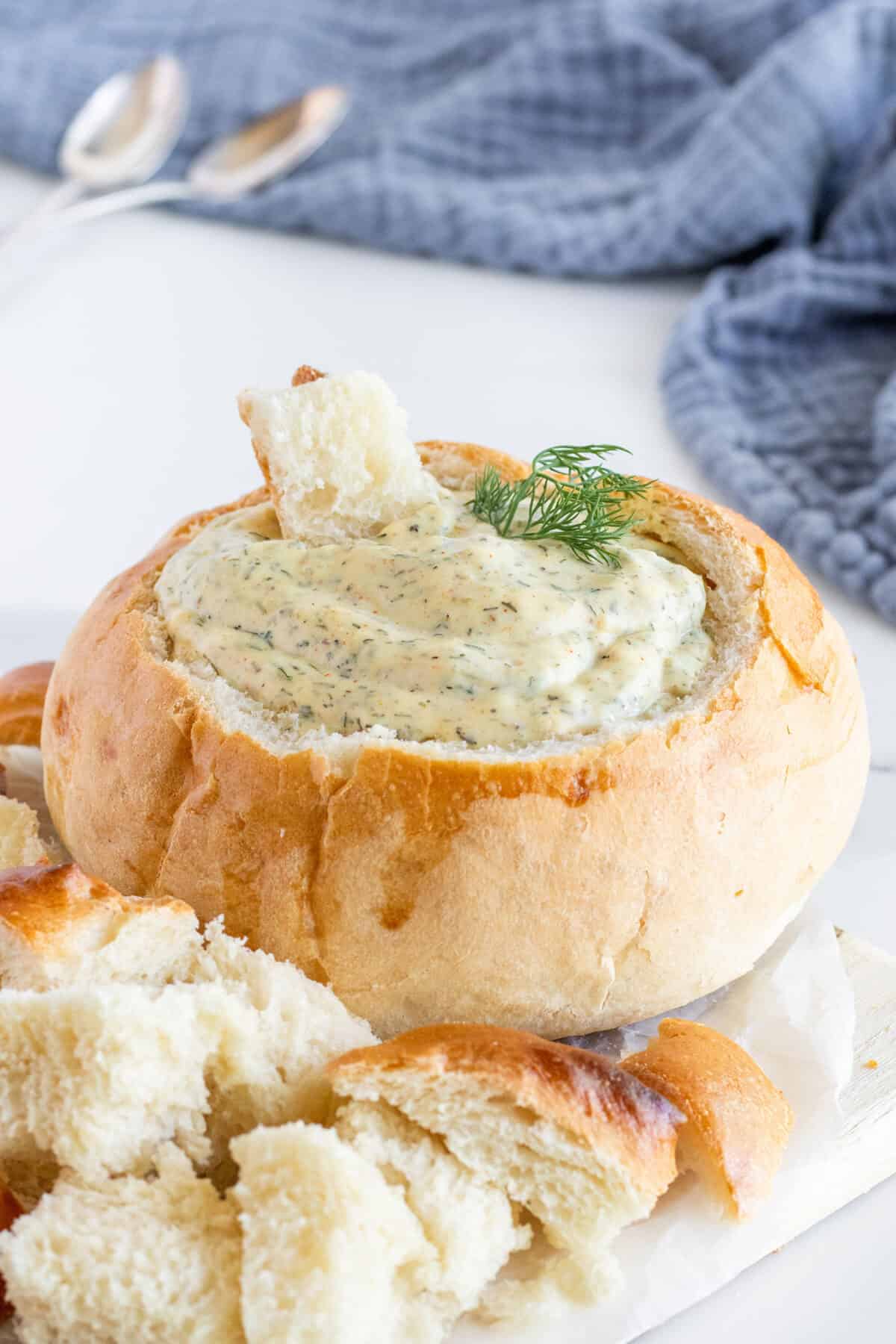 close up of dill dip in a bread bowl with a cube of bread being dunked in it