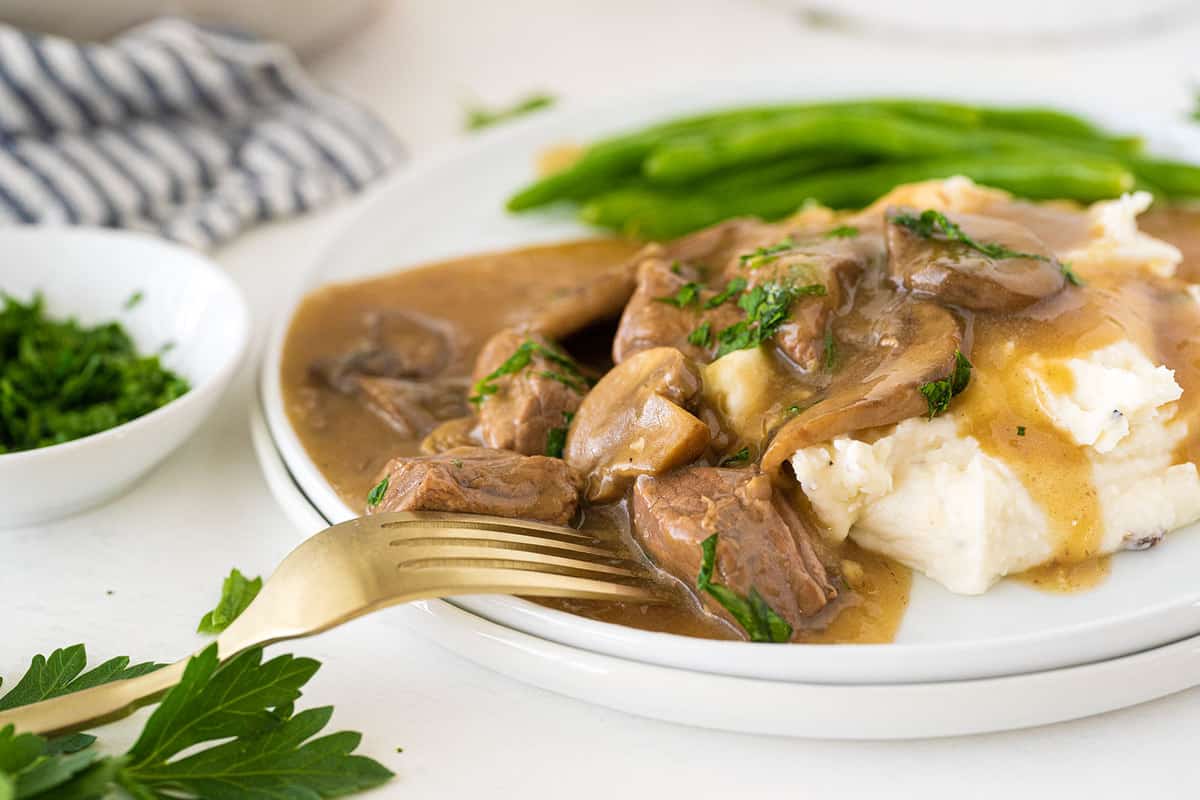 beef tips and gravy served over mashed potatoes on a white plate