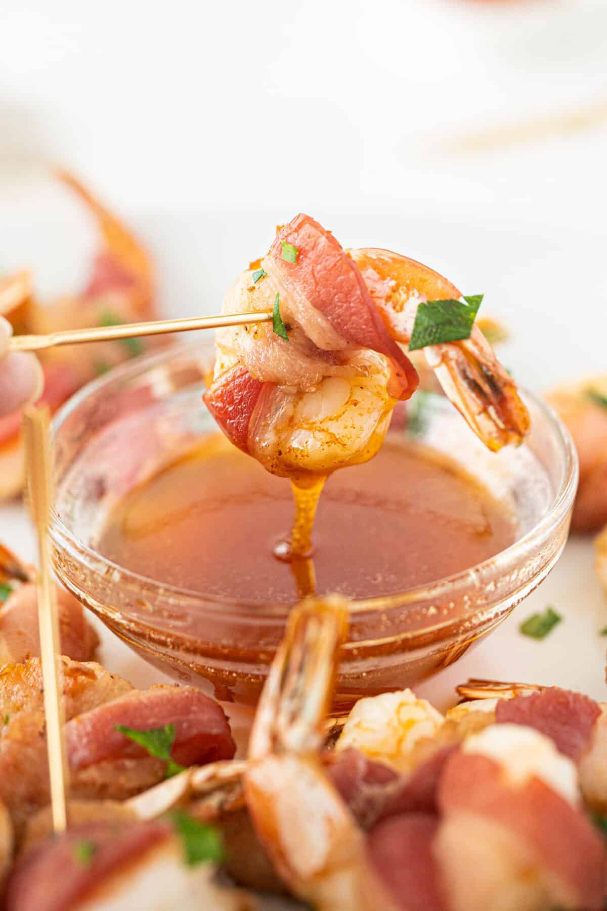 dipping a bacon wrapped shrimp into a honey hot sauce 