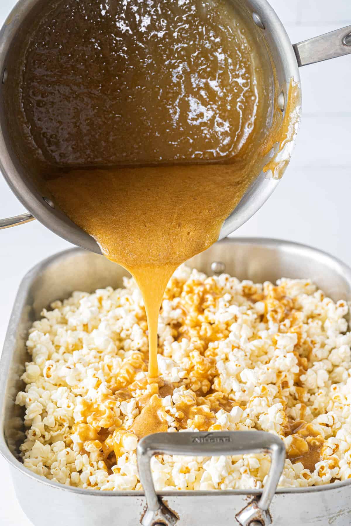 pouring caramel on popcorn in a pan