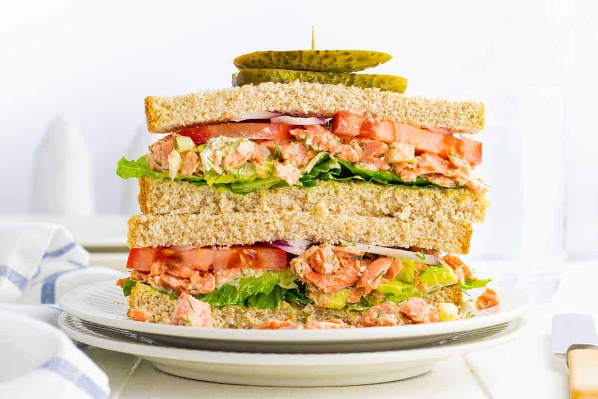  salmon salad sandwich stacked on a plate with a pickle on top