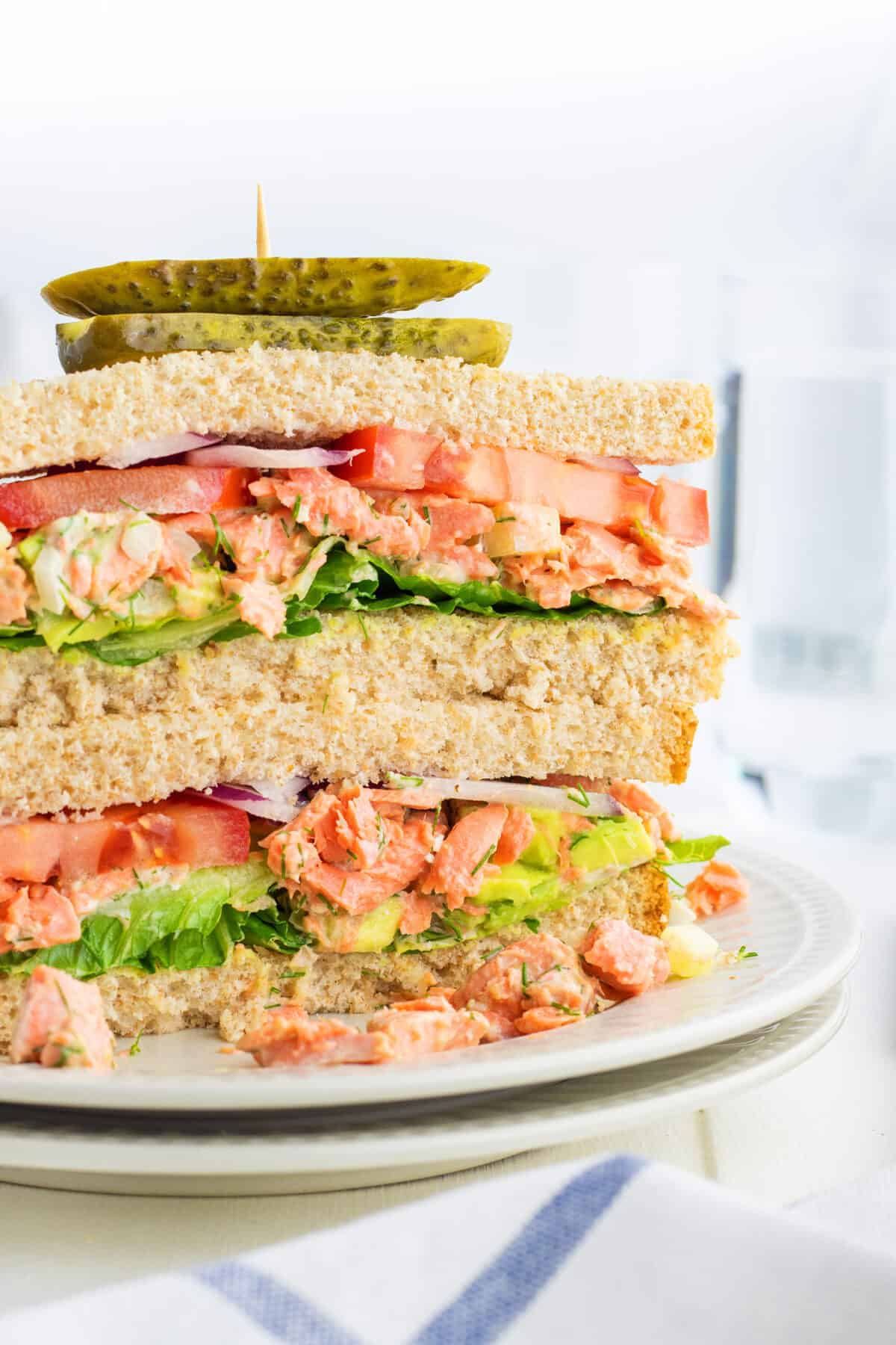  salmon salad sandwich stacked on a plate with a pickle on top