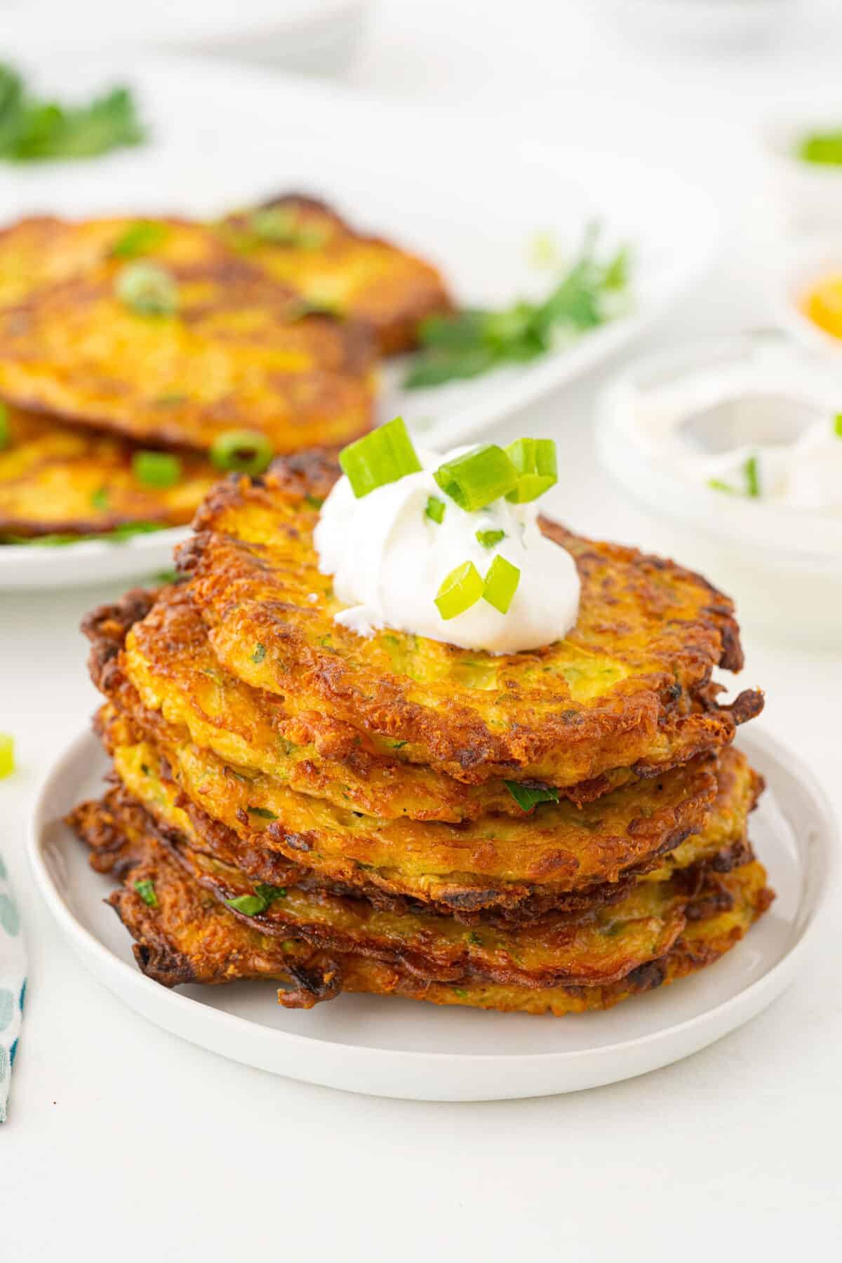 a pile of zucchini fritters on a plate with sour cream and green onions on top