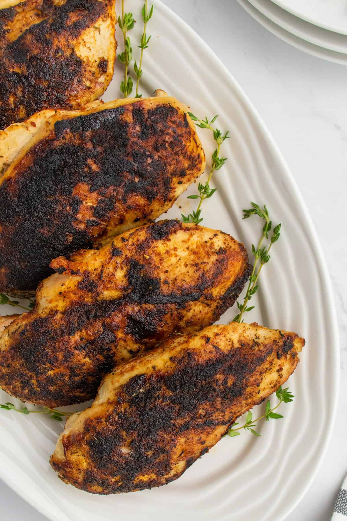 whole blackened chicken breasts on a white platter 