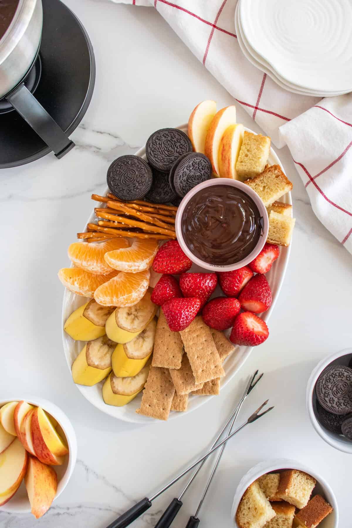 a white platter with a bowl of chocolate fondue and food