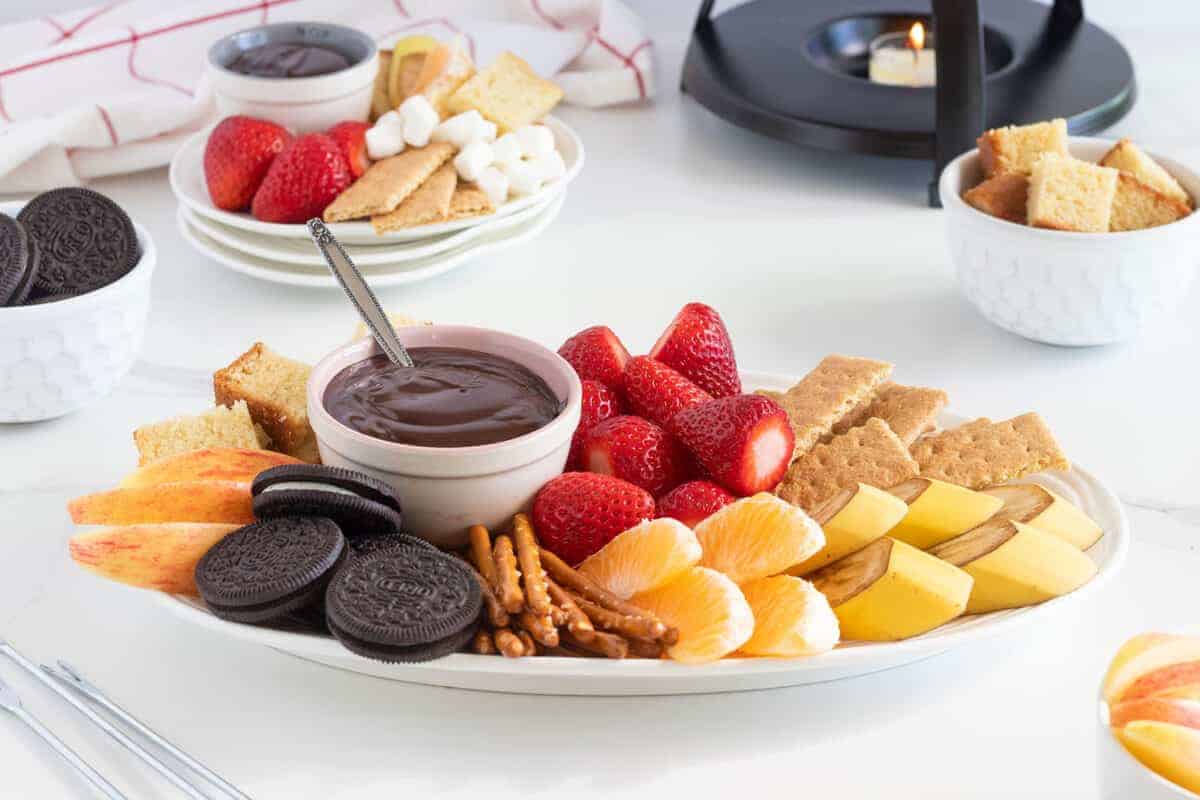 a bowl of chocolate fondue on a plate with dipping foods
