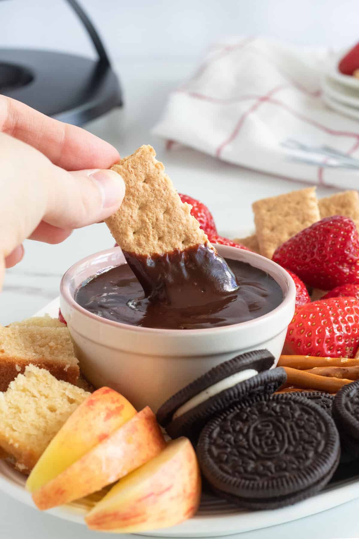 a graham cracker being dipped in chocolate fondue 