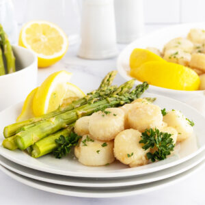 Broiled scallops on a white plate with asparagus