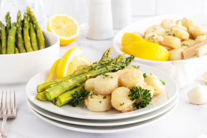 Broiled scallops on a white plate with asparagus