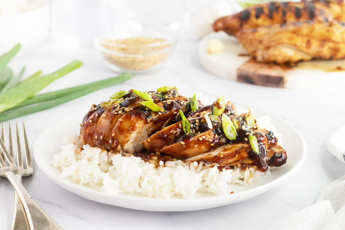 Sliced Grilled teriyaki chicken on white rice on a white plate