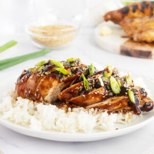Sliced Grilled teriyaki chicken on white rice on a white plate